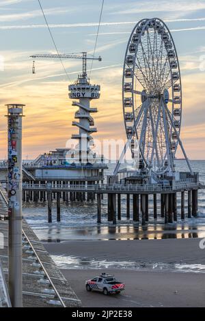 Uno scatto verticale della ruota panoramica e del Piertoren sul molo di Scheveningse con le bellissime nuvole del tramonto sullo sfondo Foto Stock