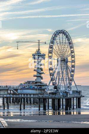 Uno scatto verticale della ruota panoramica e del Piertoren sul molo di Scheveningse con le bellissime nuvole del tramonto sullo sfondo Foto Stock