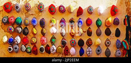 Tradizionale design marocchino lavorato a mano cappelli colorati appesi in file sul muro nel bazar medina della città - Essaouira, Marocco Foto Stock