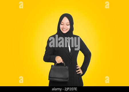 ritratto di sorridente donna musulmana asiatica d'affari che indossa una borsa da trasporto hijab mentre è in piedi isolato su sfondo giallo Foto Stock