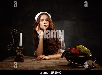 Ritratto creativo di giovane bella ragazza testa rossa con lunghi capelli ricci a immagine di persona medievale in stile rinascimentale abito isolato al buio Foto Stock