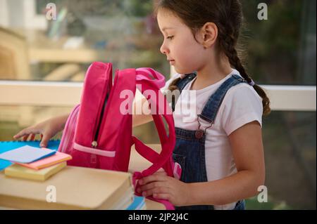 Ispirato scuola pieghevole forniture scolastiche in una rosa zaino, preparandosi per il primo grado di scuola elementare Foto Stock