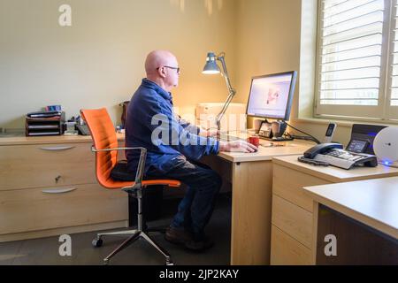 Un maschio adulto che lavora al suo computer sul posto di lavoro Foto Stock