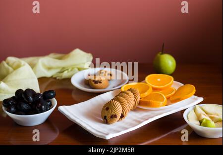 Vassoio di frutta con un mix di arance fresche, succose, dolci, pere, jamun chiamato anche bacche di prugna java e biscotti d'avena posti su un tavolo di legno scuro come b Foto Stock