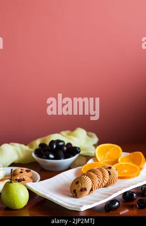 Vassoio di frutta con un mix di arance fresche, succose, dolci, pere, jamun chiamato anche bacche di prugna java e biscotti d'avena posti su un tavolo di legno scuro come b Foto Stock