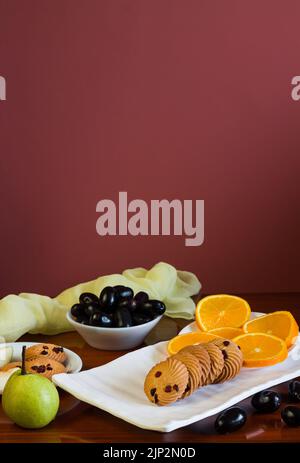 Vassoio di frutta con un mix di arance fresche, succose, dolci, pere, jamun chiamato anche bacche di prugna java e biscotti d'avena posti su un tavolo di legno scuro come b Foto Stock