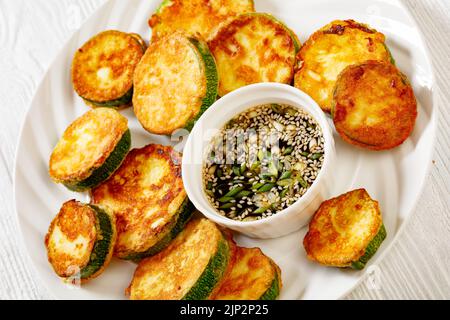 Zucchine fritte in padella in pastella di uova servite con salsa di soia su piatto su tavolo di legno bianco, Hobak Jeon, cucina coreana Foto Stock