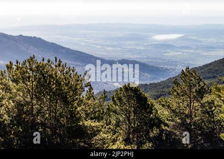 Verde paesaggio all'alba sulla valle, con alberi, rocce e vista lontana delle montagne all'orizzonte. La Morcuera, Navacerrada, Madrid. Europa. Foto Stock