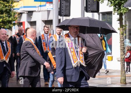 Ballymena, Regno Unito, 25th Giu 2022. Il membro di ordine arancione prende la copertura sotto l'ombrello durante la breve doccia a pioggia all'annuale mini-dodicesimo. Foto Stock