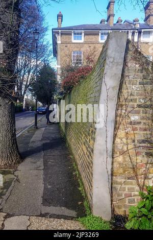 Parete in mattoni pendente che scherma un giardino privato a Londra Foto Stock