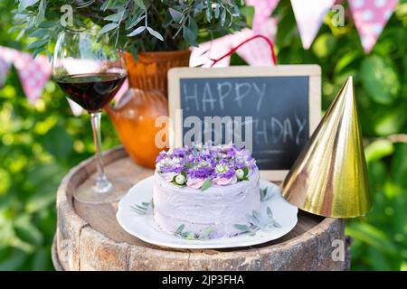 Una bellissima torta bento con fiori di viola, veri peri, mattiola su uno sfondo di bandiere rosa. Compleanno. Sullo sfondo, un bouquet di fiori Foto Stock