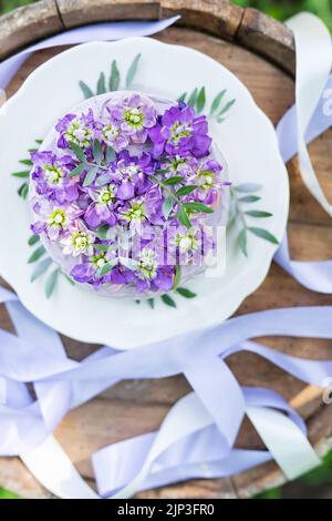 Bellissima torta bento con viola, veri peri, fiori di mattiola con foglie verdi, vista dall'alto. Compleanno, nastri belli Foto Stock