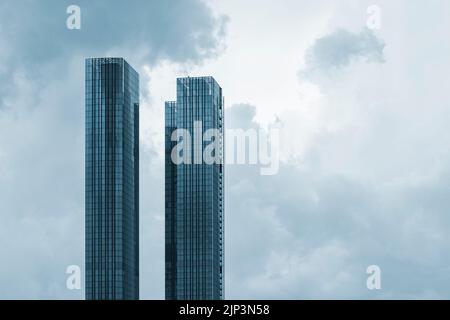 Due grattacieli in vetro e cemento contro un cielo nuvoloso. Foto dai toni. Foto Stock