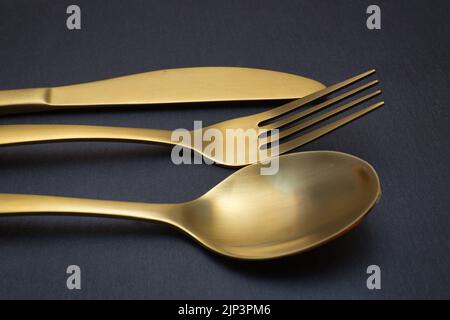 Coltello, forchetta e cucchiaio d'oro su sfondo di pietra nera - fotografia del concetto alimentare Foto Stock