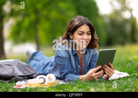 Bella giovane donna araba rilassarsi con un tablet digitale sul prato in Park Foto Stock