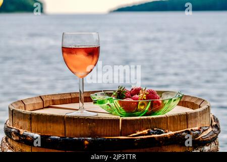 Un primo piano di un bicchiere di vino e fragole su piatto su cassetta di legno Foto Stock