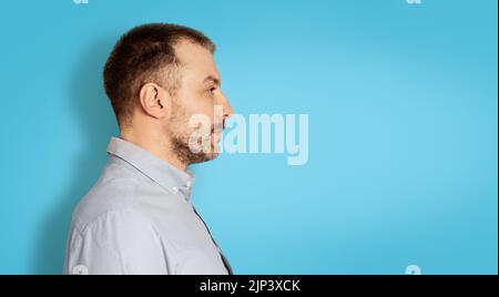 Uomo serio di mezza età che guarda da parte, sfondo blu, vista laterale Foto Stock