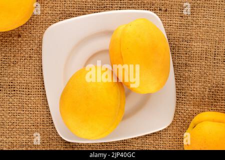 Due succulenti albicocche di ananas gialle con un piattino bianco su un tovagliolo di iuta, macro, vista dall'alto. Foto Stock