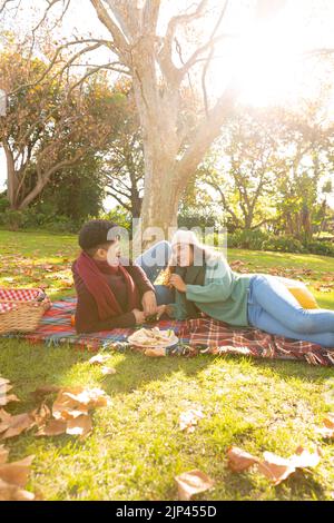 Felice coppia biraciale sdraiato su un tappeto con pic-nic e parlare nel giardino d'autunno Foto Stock