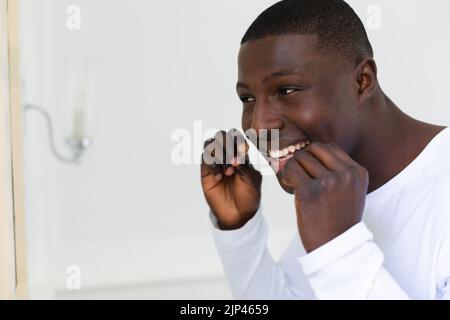 Un uomo afroamericano sorridente che gallina i denti in bagno Foto Stock