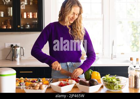 Donna caucasica sorridente in piedi in cucina tritare verdure Foto Stock