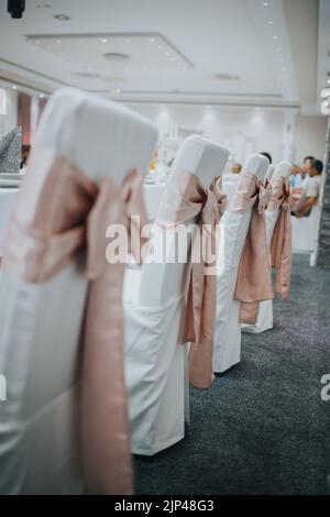 Una foto verticale di una fila di sedie bianche da sposa con nastri rosa Foto Stock