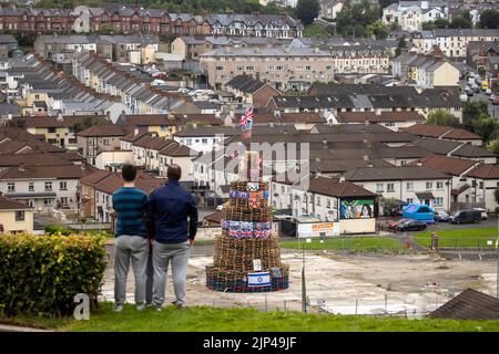 NOTA LA LINGUA SUL BANNER le persone osservano una pila di falò prima che fosse accesa per celebrare la Festa Cattolica dell'Assunzione nell'area di Bogside di Londonderry, Irlanda del Nord. Data immagine: Lunedì 15 agosto 2022. Foto Stock