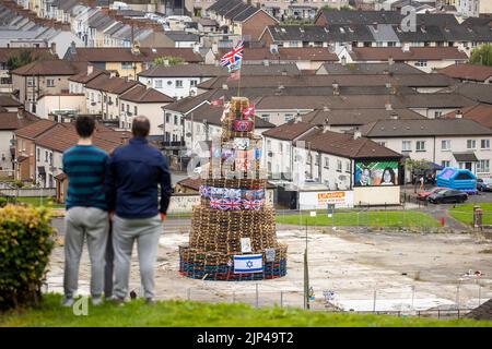 NOTA LA LINGUA SUL BANNER le persone osservano una pila di falò prima che fosse accesa per celebrare la Festa Cattolica dell'Assunzione nell'area di Bogside di Londonderry, Irlanda del Nord. Data immagine: Lunedì 15 agosto 2022. Foto Stock