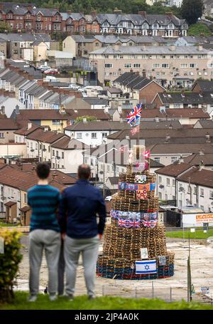 NOTA LA LINGUA SUL BANNER le persone osservano una pila di falò prima che fosse accesa per celebrare la Festa Cattolica dell'Assunzione nell'area di Bogside di Londonderry, Irlanda del Nord. Data immagine: Lunedì 15 agosto 2022. Foto Stock