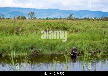 Un uomo locale in una canoa sgambata che pesca in un lago. Sulawesi, Indonesia. Foto Stock