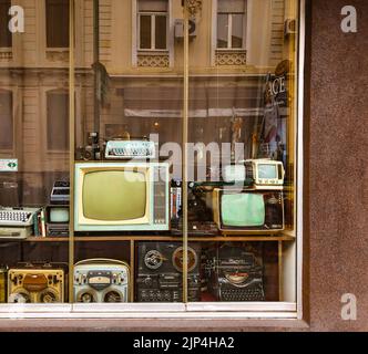 Una collezione di TV vintage, radio, macchine da scrivere e altri dispositivi dietro la finestra di un negozio di antiquariato a Bucarest, Romania Foto Stock