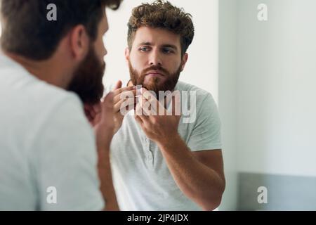 È importante controllare la pelle per individuare eventuali imperfezioni. Un bel giovanotto che controlla la pelle nello specchio del bagno. Foto Stock