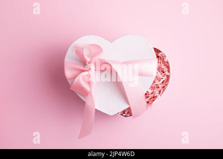 Confezione regalo bianca a forma di cuore, isolata su sfondo rosa pastello. Giorno della donna, biglietto di auguri di San Valentino. Foto Stock