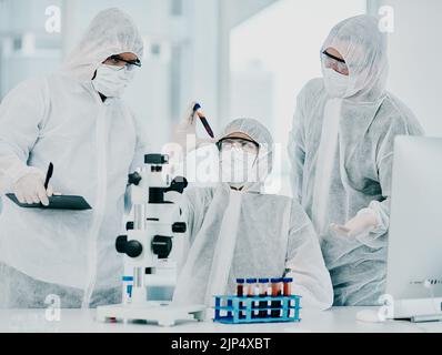 Gruppo di medici e scienziati che conducono una ricerca medica sui virus vestiti in tute di nocciola, per la cura del coronavirus nel laboratorio. Ricercatori Foto Stock