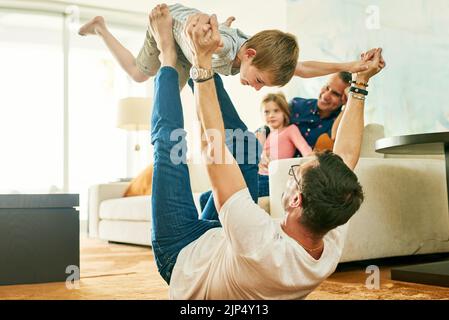 Più in alto, più in alto, un adorabile ragazzino che gioca con il padre a casa. Foto Stock