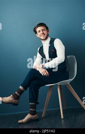 Cercando il pugnalatore nel suo abbigliamento di affari. Studio shot di un bel giovane uomo d'affari che posa su uno sfondo blu. Foto Stock
