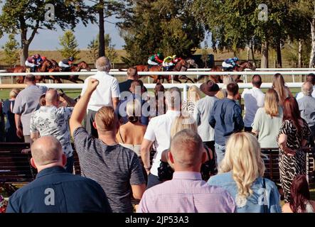 Uomo vincente che alza il pugno in aria, mentre gli applausi di spettatori e punter felici alle gare di Newmarket July, Newmarket, Suffolk, Inghilterra, Regno Unito Foto Stock