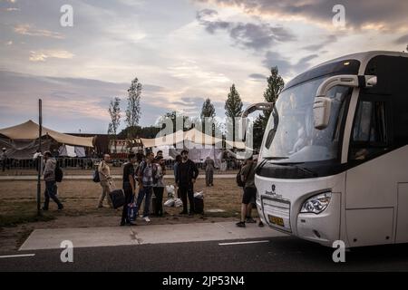 2022-08-15 20:52:11:19 ter APEL - i richiedenti asilo aspettano un autobus per un rifugio di emergenza al di fuori del rifugio di fortuna al di fuori del cancello del centro dei richiedenti asilo COA quando si sta sviluppando un temporale. L'Agenzia centrale per l'accoglienza dei richiedenti asilo (COA) prevede che circa 150 persone dovranno dormire all'esterno presso il centro di applicazione di Ter Apel a causa della folla. ANP VINCENT JANNINK olanda fuori - belgio fuori Foto Stock