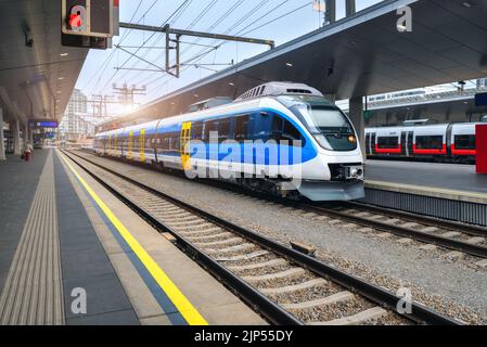 Treno ad alta velocità alla stazione ferroviaria al tramonto a Vienna, Austria. Bel treno passeggeri interurbano blu moderno sulla piattaforma ferroviaria. Ferrovia Foto Stock