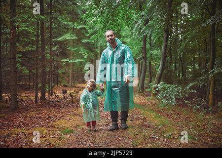 Padre e figlia in impermeabile camminano nella foresta serale Foto Stock