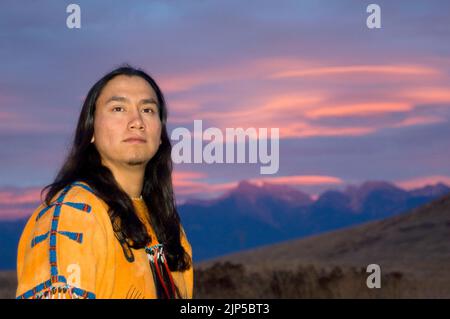 Primo piano del ragazzo dei nativi americani indossa una camicia tradizionale con perline e tramonto sulla catena montuosa Foto Stock