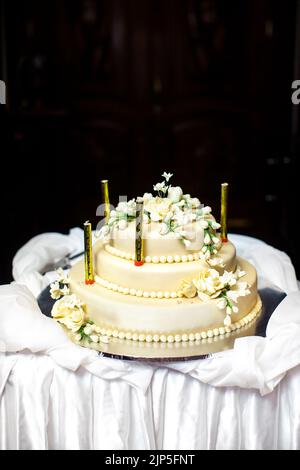 Torta nuziale multilivello decorata con fiori e candele. Foto Stock