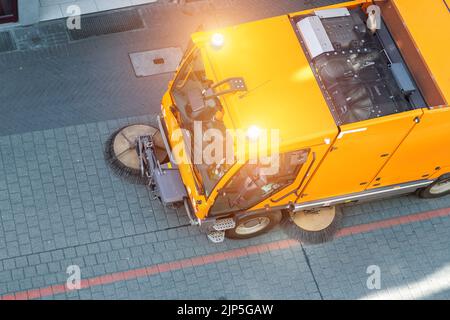 Vista dall'alto di un piccolo aspirapolvere spazzante macchina attrezzatura di rimozione polvere rifiuti strada strada strada strada lastricata vicino condominio edificio appartamento Foto Stock