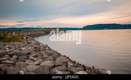 Una vista della gente su una riva rocciosa di un lago sotto il cielo nuvoloso Foto Stock