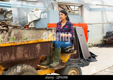 Donna contadina latinoamericana che guida un camion mini dump, guida fuori per buttare via le erbacce. Foto Stock