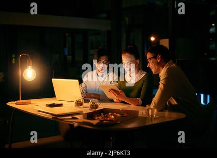 Le lunghe ore di lavoro di squadra non hanno niente a che vedere con il lavoro di squadra. Gli uomini d'affari lavorano insieme su un tablet digitale in ufficio di notte. Foto Stock