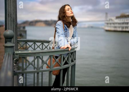 Ritratto senza posa della giovane donna pensierosa sul molo che si affaccia sulla baia di San Francisco Foto Stock