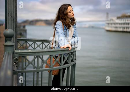 Ritratto senza posa della giovane donna pensierosa sul molo che si affaccia sulla baia di San Francisco Foto Stock