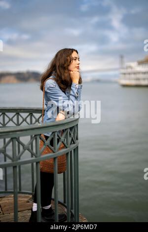 Ritratto senza posa della giovane donna pensierosa sul molo che si affaccia sulla baia di San Francisco Foto Stock