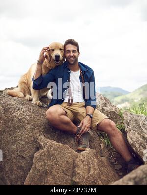 Mans migliore amico per la vita. Un bel giovane seduto su una roccia con il suo recupero d'oro dopo una giornata di escursioni. Foto Stock